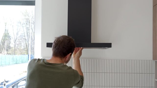 Back view of man replacing extractor hood filter in modern kitchen interior. Concept of DIY repair home maintenance and kitchen appliance care.