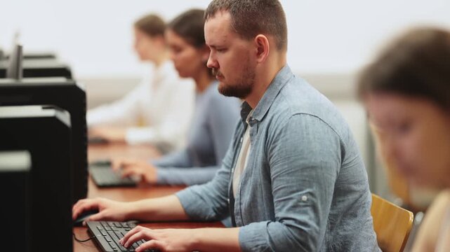 Side view on concentrated male student sitting at library desk with pc, preparing for exam in computer class. High quality 4k footage