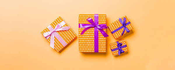 Naklejka premium wrapped Christmas or other holiday handmade present in paper with purple and pink ribbon on orange background. Present box, decoration of gift on colored table, top view