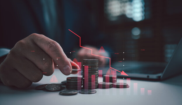 Hand arranging coin stacks beside a falling red chart on desk, symbolizing financial crisis, investment warning, stock market decline, low returns, capital loss, and business risk concept.