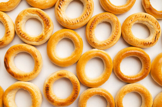 Background of scattered mini bagels. Close-up of freshly baked mini dry bagels, pattern of round cookies on white background top view. Food background, baked goods for tea
