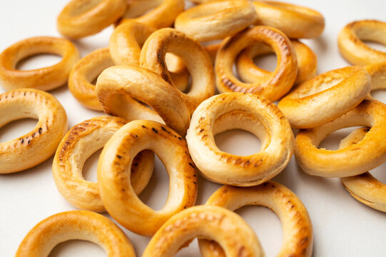Background of scattered mini bagels. Close-up of freshly baked mini dry bagels, pattern of round cookies on white background top view. Food background, baked goods for tea