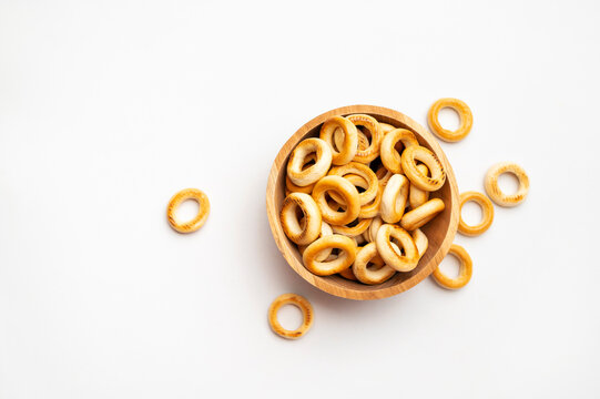 Small bagels in wooden bowl on white background, top view. Freshly baked round mini buns, dry cookies for tea, delicious flour-based pastries