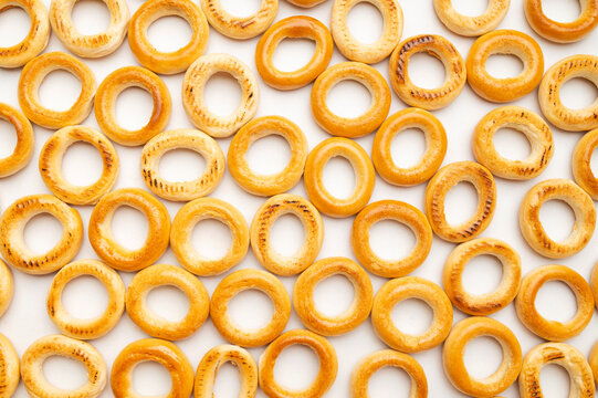 Background of scattered mini bagels. Close-up of freshly baked mini dry bagels, pattern of round cookies on white background top view. Food background, baked goods for tea
