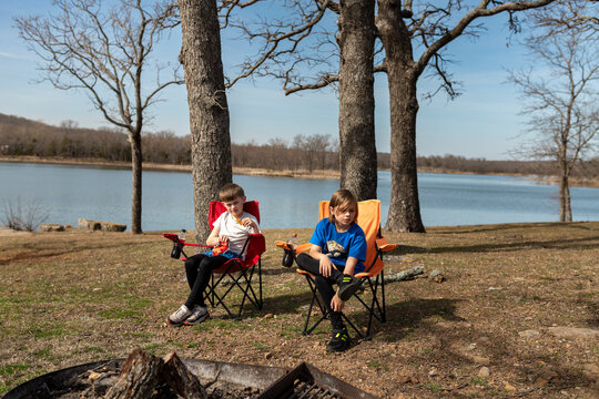 two boys sitting in chairs eating at lakeside campsite
