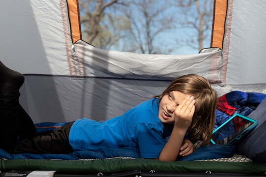 Young boy lying in a tent on a sleeping bag with tablet