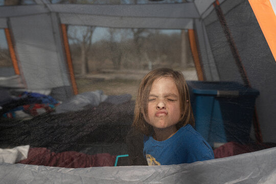 Young boy making a funny face pressed against a mesh tent screen