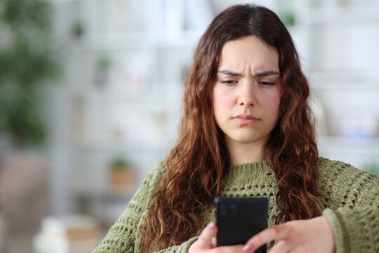 Confused teenage girl checking cell phone at home