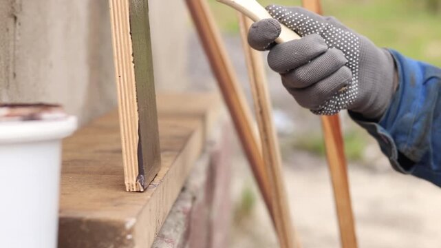 Painter covers a wooden panel with brown varnish, close-up. Hand in a protective glove holds a brush, painting a wooden surface. Handmade. The process of treating wood with a protective coating