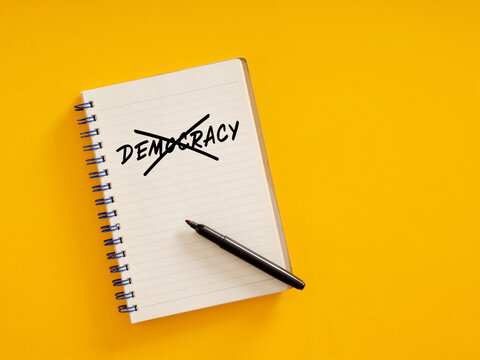 Notebook with crossed out democracy writing on yellow background