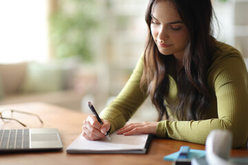 Student learning taking notes on a wooden table at home © Antonioguillem