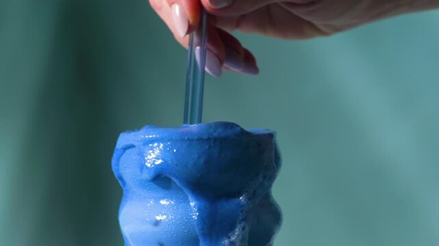 Hand stirring vivid blue spirulina latte causing dramatic overflow in wavy bubble glass perfect as visual hook for social media ads
