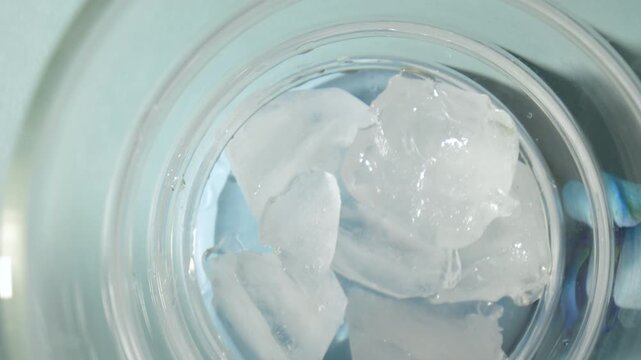Top view overhead shot of crystal clear ice cubes dropping into empty wavy bubble glass for cocktail or spirulina latte preparation