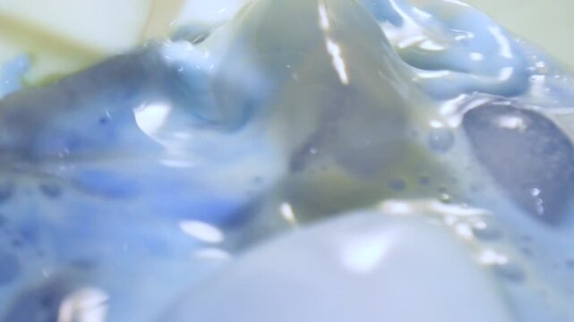 Extreme macro slow motion shot of blue spirulina milk pouring over crystal ice cubes with vivid color swirl and liquid texture detail