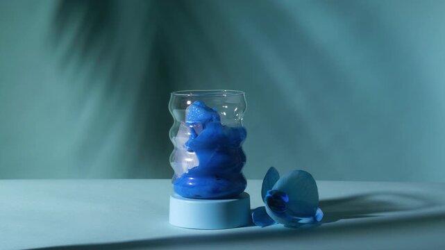 Vivid blue spirulina milk pouring from pitcher over crystal ice into wavy bubble glass beside orchid on teal surface in slow motion