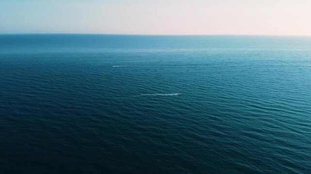 High aerial drone shot over the open Mediterranean Sea. Two small boats cross the frame in opposite directions, leaving faint white wakes on the deep blue water under a soft pastel horizon.
