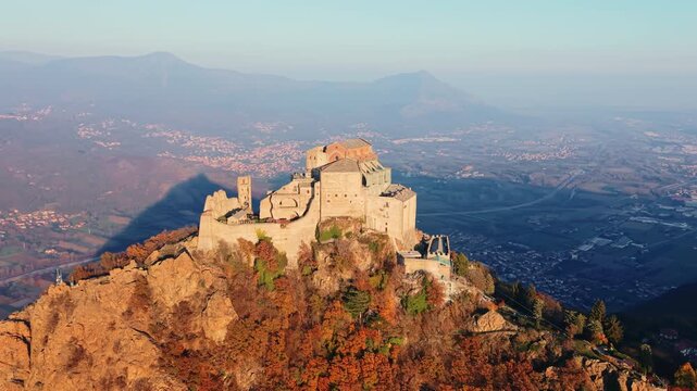 Aerial: sunset view of Saint Michael's Abbey with golden hour colors in Sant'Ambrogio di Torino, Piedmont, Italy, orbit drone shot