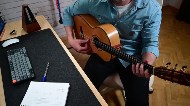 Mature man playing classical guitar at home studio desk