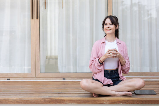 A woman enjoys her coffee while sitting cross-legged on a porch