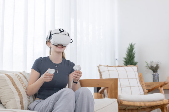 Young woman enjoys virtual reality experience at home while using VR headset and controllers in a cozy living room