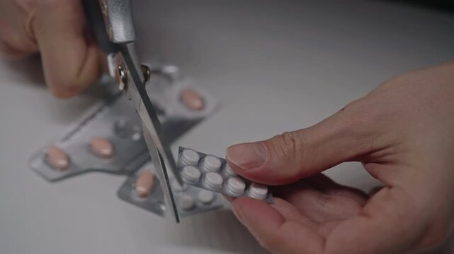 Person hands using scissors to cut medication blister pack, dividing daily doses of pills on white table for health treatment, medication management. Concept of healthcare, wellness, medical therapy.