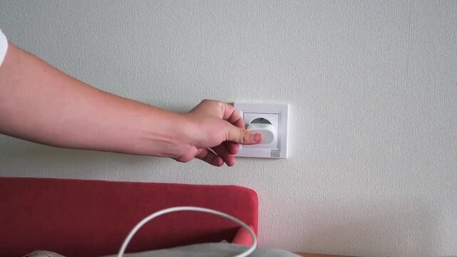 Hand plugging a white USB power adapter into a wall electrical socket at home