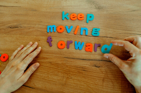 Hand placing letters to spell keep moving forward on wooden table