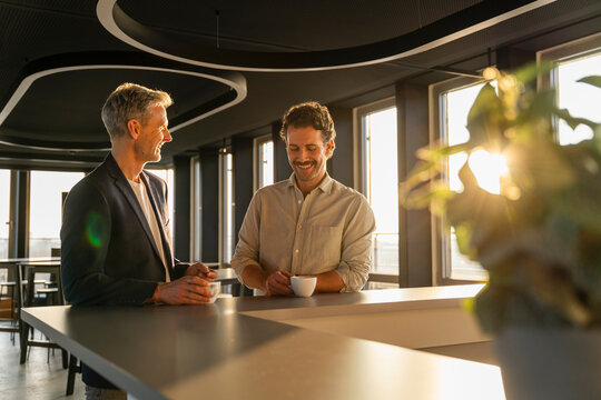 Two men having a business meeting with coffee in a modern office at sunset