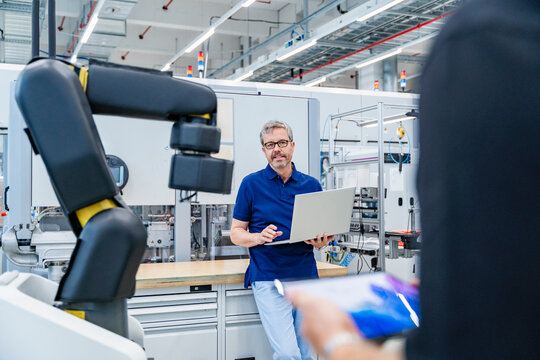 Engineer with laptop in modern factory with industrial robot during meeting