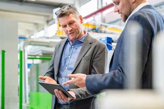 Businessman and manager discuss on tablet in production hall
