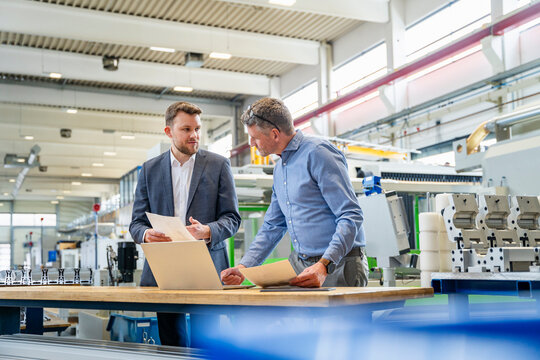 Engineers discussing production plans with laptop at factory