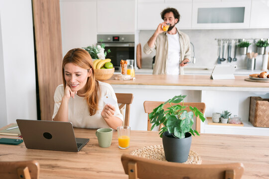 Smiling woman paying online with credit card at home in kitchen