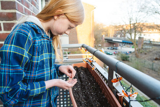 Girl planting seed in a balcony planter box for urban farming