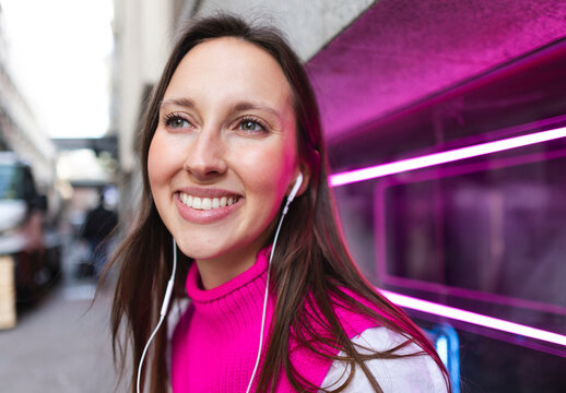 Smiling woman in pink sweater listening to music in the city