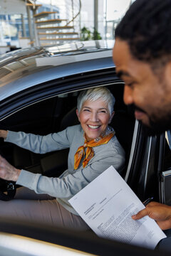 Smiling salesperson holding document near customer sitting in car
