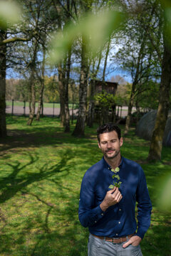 Smiling businessman holding twig and standing with eyes closed in back yard garden