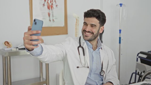 Man doctor with stethoscope smiling and taking a selfie with a smartphone, holding phone in hand inside a building; compassion trust.