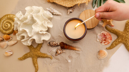 Lighting a scented candle surrounded by beach treasures and seashells on sand © shine.graphics