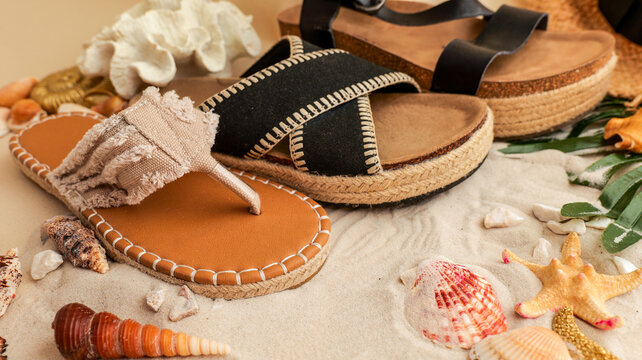 Stylish espadrille sandals and flip-flops resting on a sandy beach with seashells