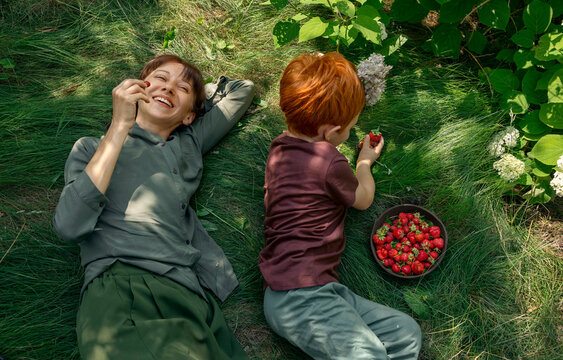 Mother and son eating strawberry on grass in the garden