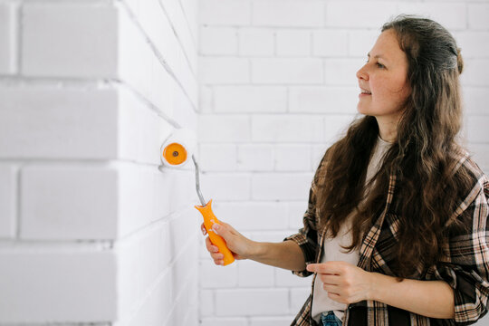 Woman decorating a white brick wall indoors with a paint roller