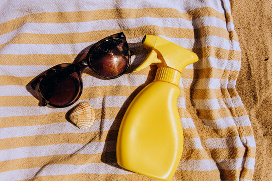 Sunscreen spray, eyewear and shell on a striped beach towel