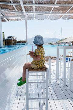 Girl relaxing at seaside cafe in summer with drink and hat
