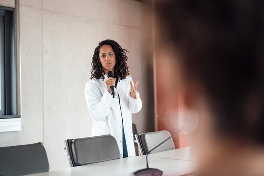 Confident young female doctor explaining through microphone in board room at hospital