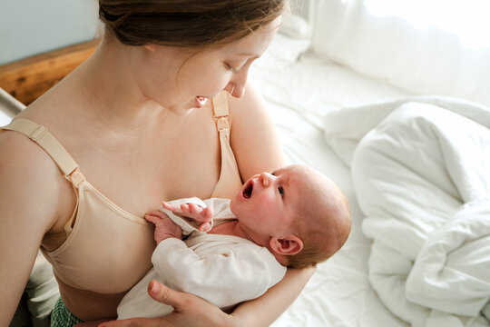 Mother holding yawning newborn baby on bed at home