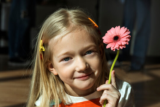 Child smiling indoors holding a flower in natural light portrait