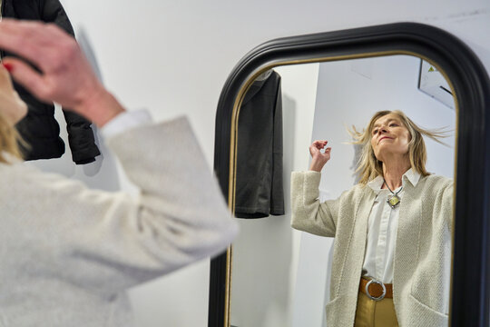 Woman looking in the mirror indoors adjusting hair with optimism
