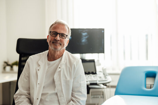 Smiling doctor in white coat sitting in modern hospital clinic