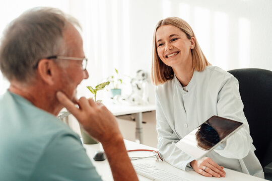 Smiling doctor showing tablet to patient during indoor consultation