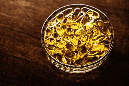 Glass bowl filled with golden omega 3 fish oil capsules on wood